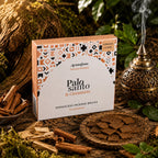 Boîte d'encens Aromafume Palo Santo & Cinnamon entourée de bâtons de cannelle et de morceaux de Palo Santo, avec des briques d'encens fines étalées sur un plateau sculpté et un brûleur oriental.