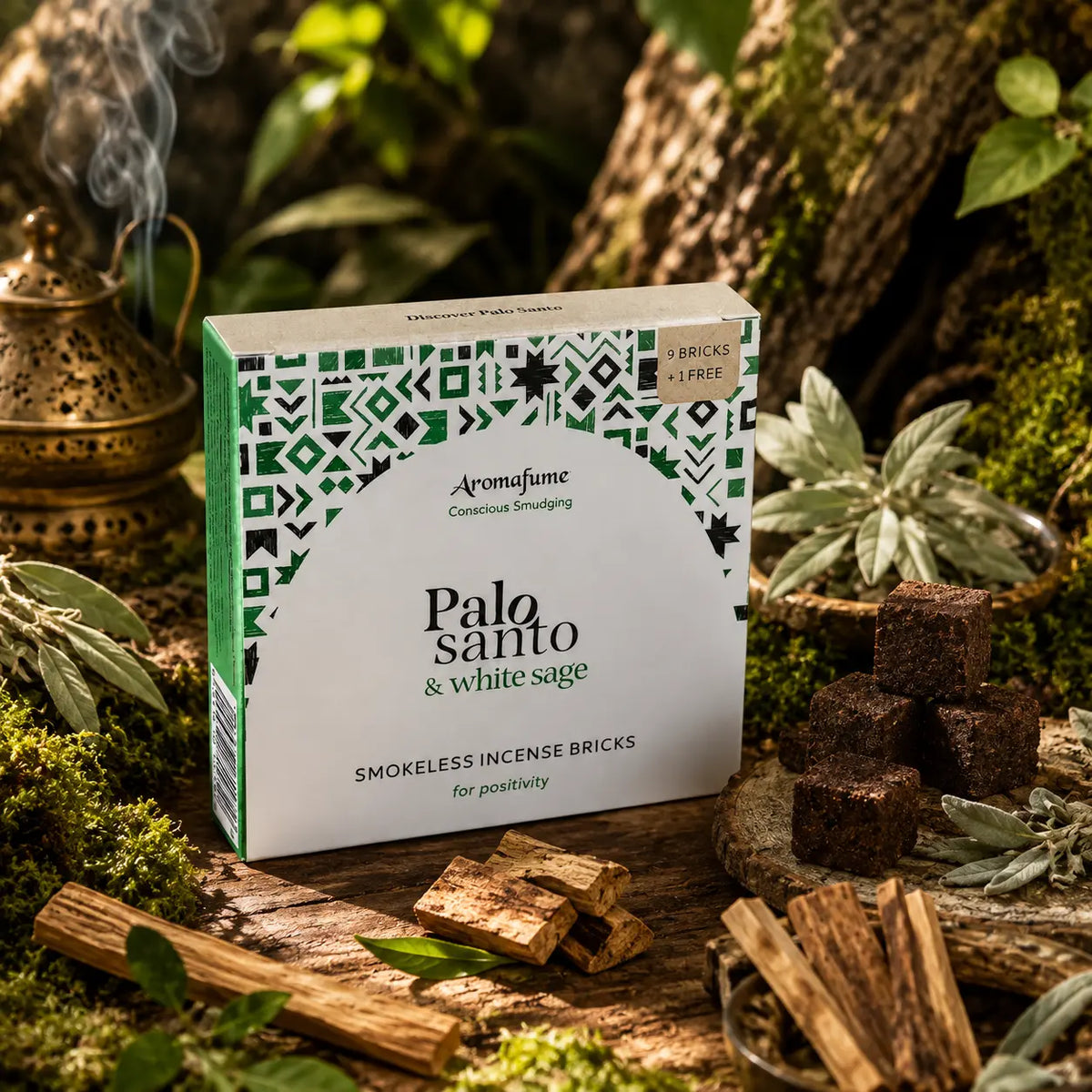 Boîte d'encens Aromafume Palo Santo & White Sage posée au milieu de feuilles de sauge blanche et de bâtonnets de Palo Santo, avec des briques d'encens carrées et un brûleur doré.