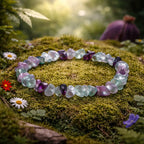 Bracelet d'éclats baroques translucides de fluorite aux nuances violettes et vertes, reposant sur un tapis de mousse forestière parsemé de fleurs.