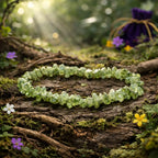 Bracelet composé de petits éclats de péridot vert olive translucide et étincelant, posé sur une écorce de bois ancienne parmi des fleurs sauvages baignées de soleil.