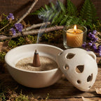 Brûle-encens en céramique blanche, forme goutte ajourée, pour cônes d’encens, présenté ouvert sur décor naturel.