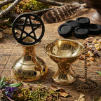 Brûle-encens/encensoir doré en laiton avec chaînette, posé sur une table en bois, accompagné d’un support avec symbole pentagramme et de charbons noirs, plumes et résine d’encens en arrière-plan.