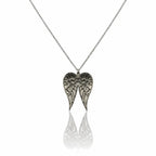 Pendentif en forme de deux ailes d'ange détaillées en argent vieilli, suspendu à une fine chaîne sur fond blanc.