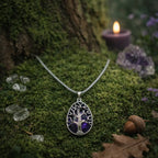 Pendentif goutte argenté ciselé d'un arbre de vie protecteur sur une pierre d'améthyste violette, posé sur de la mousse épaisse à côté d'un gland et d'une bougie.