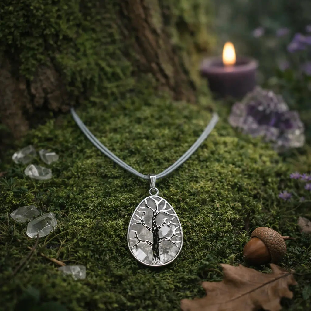 Pendentif en forme de goutte argentée ciselée d'un arbre de vie sur un fond de cristal de roche translucide, déposé sur de la mousse fraîche près d'une bougie allumée.