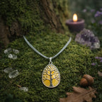Pendentif goutte argenté ciselé d'un arbre de vie protecteur sur une pierre de jade jaune miel translucide, posé sur de la mousse forestière parsemée de cristaux de quartz.