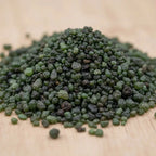Gros plan sur un tas de grains d’encens à la sauge verts et foncés sur fond en bois.
