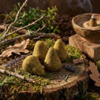 Cônes d’encens verts posés sur une tranche de bois, avec porte-encens en céramique fumant, mousse, branches, feuilles et brins de lavande.