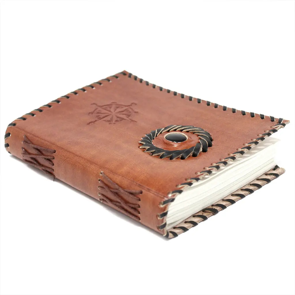 Un carnet grimoire en cuir marron posé à plat, bordé d'un tressage en cuir noir et orné d'une rose des vents ainsi que d'une pierre d'onyx centrale, sur fond blanc.