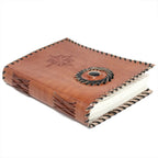 Un carnet grimoire en cuir marron posé à plat, bordé d'un tressage en cuir noir et orné d'une rose des vents ainsi que d'une pierre d'onyx centrale, sur fond blanc.