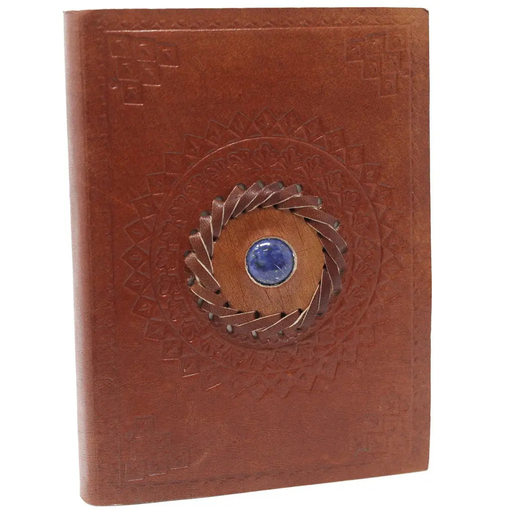 La couverture d'un carnet grimoire en cuir marron clair, ornée d'une pierre de lapis-lazuli bleue centrale sertie dans une tresse de cuir et entourée de motifs mandalas embossés, sur fond blanc.