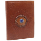 La couverture d'un carnet grimoire en cuir marron clair, ornée d'une pierre de lapis-lazuli bleue centrale sertie dans une tresse de cuir et entourée de motifs mandalas embossés, sur fond blanc.