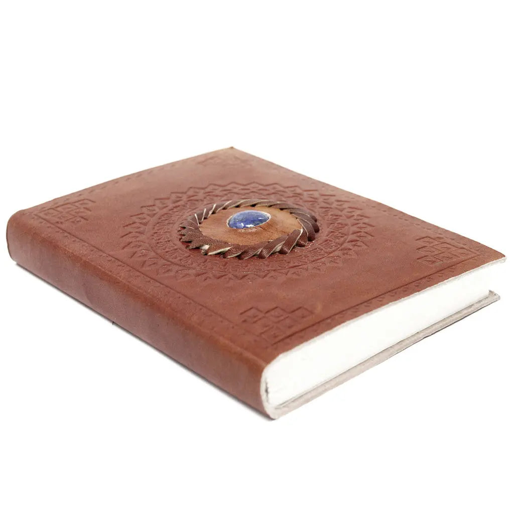 Un carnet grimoire en cuir marron clair posé à plat, orné d'une pierre de lapis-lazuli bleue centrale sertie dans une tresse de cuir et entouré de motifs mandalas embossés, sur fond blanc.