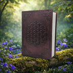 Grimoire en Cuir Artisanal - Fleur de Vie en cuir marron avec géométrie sacrée embossée, posé sur une branche moussue entourée de fleurs violettes en forêt.