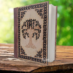 Un carnet grimoire entrouvert présentant un dos en cuir marron et une couverture en bois ciselée d'un arbre de vie et d'entrelacs celtiques, posé sur un support en bois.