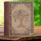 La couverture d'un carnet grimoire associant un dos en cuir marron et une plaque de bois finement sculptée d'un arbre de vie central et de bordures celtiques, présentée sur un support en bois.