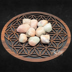 Pierres de morganite polies, aux douces nuances de rose et de pêche, disposées sur une fleur de vie en bois.