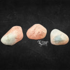 Trois pierres de morganite polies, aux nuances de rose et de pêche, présentées sur un fond noir.