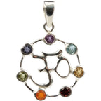 Un pendentif Om en argent au centre d'un cercle serti de sept pierres naturelles taillées aux couleurs des chakras, surmonté d'une bélière, sur fond blanc.