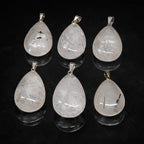 Un ensemble de six pendentifs en cristal de roche en forme de goutte, chacun présentant des inclusions de tourmaline noire uniques, surmontés de bélières en métal argenté et disposés avec leurs reflets sur un fond noir.