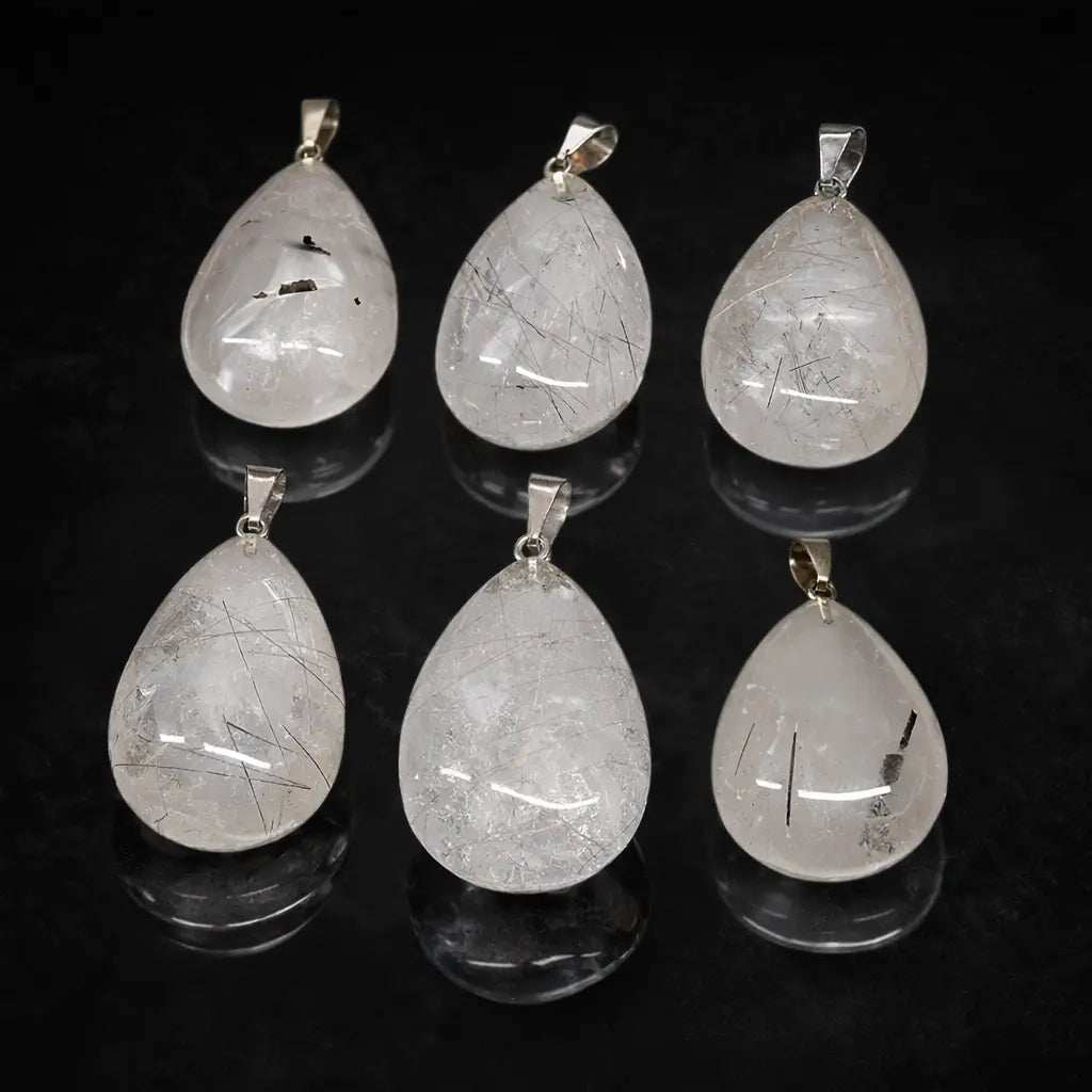 Un ensemble de six pendentifs en cristal de roche en forme de goutte, chacun présentant des inclusions de tourmaline noire uniques, surmontés de bélières en métal argenté et disposés avec leurs reflets sur un fond noir.