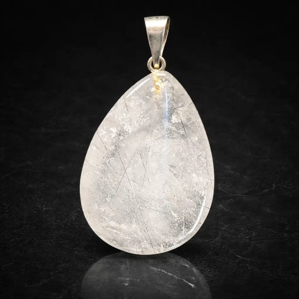 Un pendentif en cristal de roche taillé en forme de goutte, contenant des inclusions de tourmaline noire (quartz tourmaline), surmonté d'une bélière en métal argenté et présenté sur un fond sombre.
