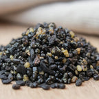 Gros plan sur un monticule de grains d'encens Pontifical, montrant un mélange de morceaux de résine noire brillante et de larmes de résine jaune clair/ambre.