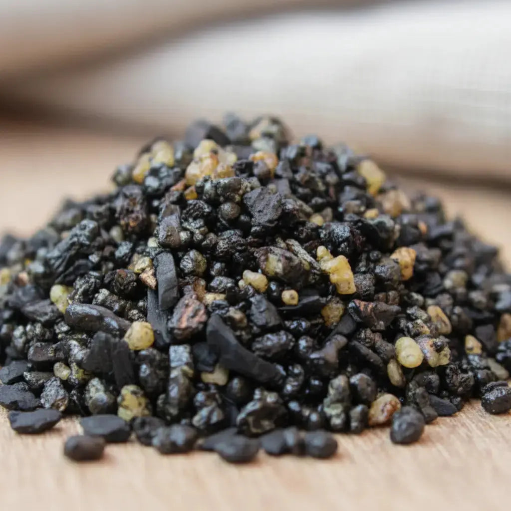 Gros plan sur un monticule de grains d'encens Pontifical, montrant un mélange de morceaux de résine noire brillante et de larmes de résine jaune clair/ambre.