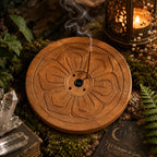 Porte encens bois rond - Motif Taillé Fleur posé sur un lit de mousse forestière, accueillant un bâtonnet en cours de combustion à côté de pointes de cristal de roche.