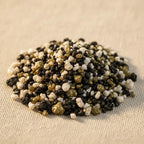 Gros plan sur des grains d’encens Prière aux défunts noirs, blancs et dorés disposés en tas sur tissu clair.
