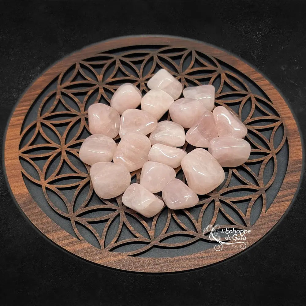 Un groupe de pierres de quartz rose roulées aux surfaces lisses et brillantes, présentant une couleur rose tendre, disposé sur un plateau en bois orné du symbole de la "Fleur de Vie".