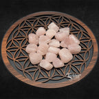 Un groupe de pierres de quartz rose roulées aux surfaces lisses et brillantes, présentant une couleur rose tendre, disposé sur un plateau en bois orné du symbole de la "Fleur de Vie".