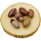 Plusieurs pierres Shiva Lingam (5-6 cm) de forme ovoïde, ornées de bandes naturelles brunes et grises, disposées sur une tranche de bois clair.