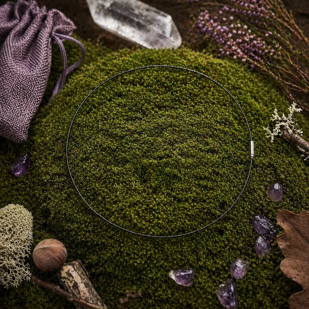Câble gainé noir circulaire avec fermoir argenté, posé sur une butte de mousse avec une pointe de cristal, une pochette violette et des pierres d'améthyste.