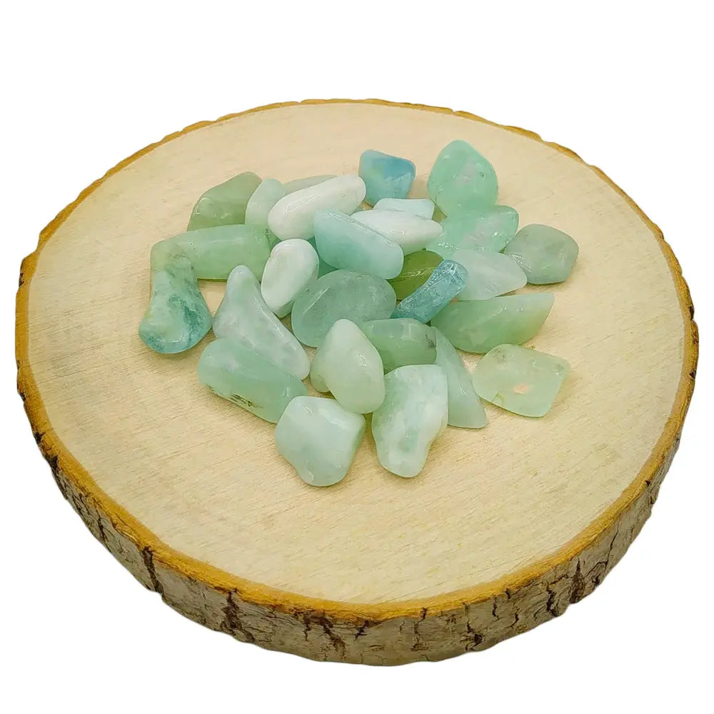 Un tas de petites pierres d'aigue-marine roulées aux nuances vert d'eau et bleu pâle translucides, disposé sur une rondelle de bois clair.