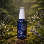 Flacon bleu à pompe d'Huile Végétale Amande Douce Apaisante Herbes et Traditions posé sur un lit de mousse avec des fleurs de lavande en arrière-plan.