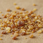 Gros plan sur des grains de résine d’encens ambre dorés et ambrés sur fond sable clair.