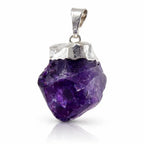 Un pendentif en améthyste brute d'un violet profond, serti sur sa partie supérieure par une calotte et une bélière en métal argenté, présenté avec son reflet sur un fond blanc.