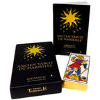 Coffret « Ancien Tarot de Marseille » (Grimaud) : deux boîtes noires avec un soleil doré et lettrage doré, dont une étui vertical « ANCIEN TAROT DE MARSEILLE » ; au premier plan, une carte du tarot « LE MAT » est partiellement sortie du coffret (Éditions TrajectoirE).