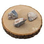 Trois morceaux d'angélite brute aux nuances bleu-gris et blanches, présentés sur une tranche de bois clair.