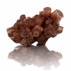 Un cristal d'aragonite brut présentant un agrégat de prismes hexagonaux aux teintes brunes et orangées, posé sur un fond blanc avec un reflet net.