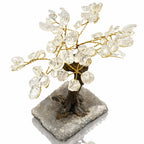Un arbre du bonheur décoratif aux feuilles en pierres de cristal de roche et branches dorées, s'élevant d'un socle rectangulaire recouvert de petits cristaux, présenté sur un fond blanc.