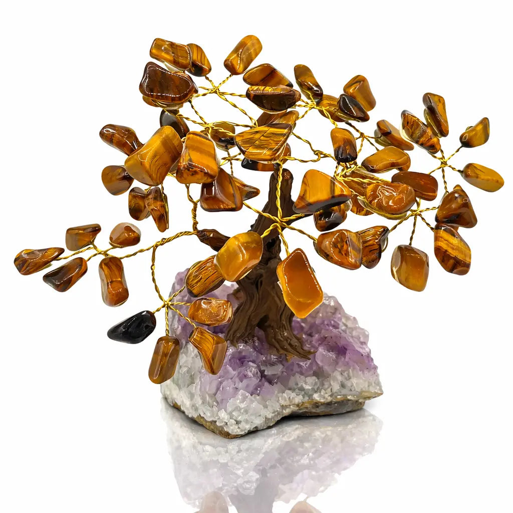Un arbre du bonheur décoratif aux feuilles en pierres d'œil de tigre et branches dorées, s'élevant d'un socle en amas de cristaux d'améthyste brute, présenté sur un fond blanc.