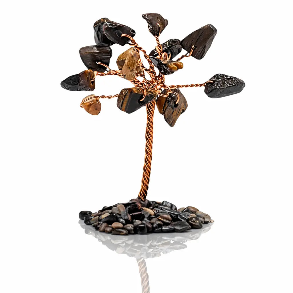 Un arbre du bonheur décoratif miniature composé d'un tronc en fil de cuivre torsadé et de feuilles en pierres d'œil de tigre, fixé sur un socle de petits éclats minéraux sombres, présenté sur fond blanc.