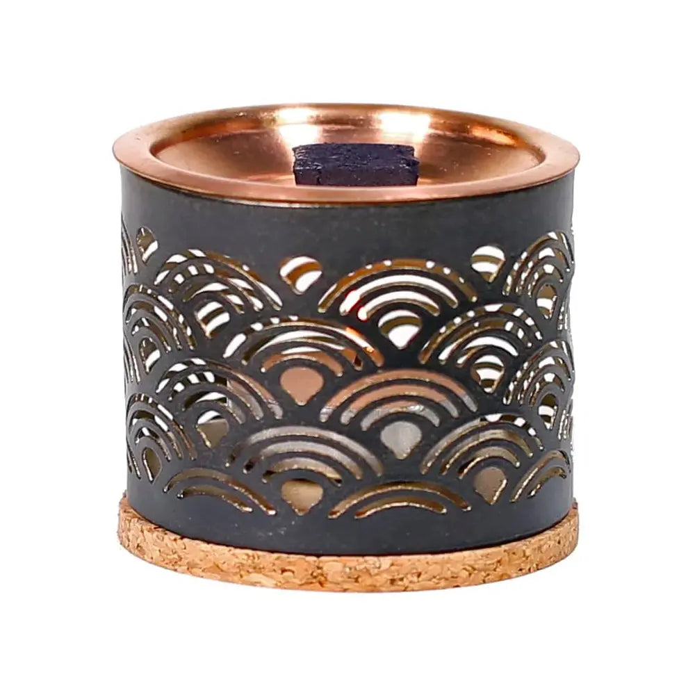 Diffuseur à encens en métal gris foncé, décor ajouré en arcs, coupelle cuivrée avec brique d’encens, base liège, sur fond blanc.
