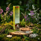 Boîte d'encens Saint Georges Aromatika de couleur verte, posée sur une tranche de bois dans une forêt, entourée de sauge blanche séchée, d'une bougie et d'un bâtonnet fumant.