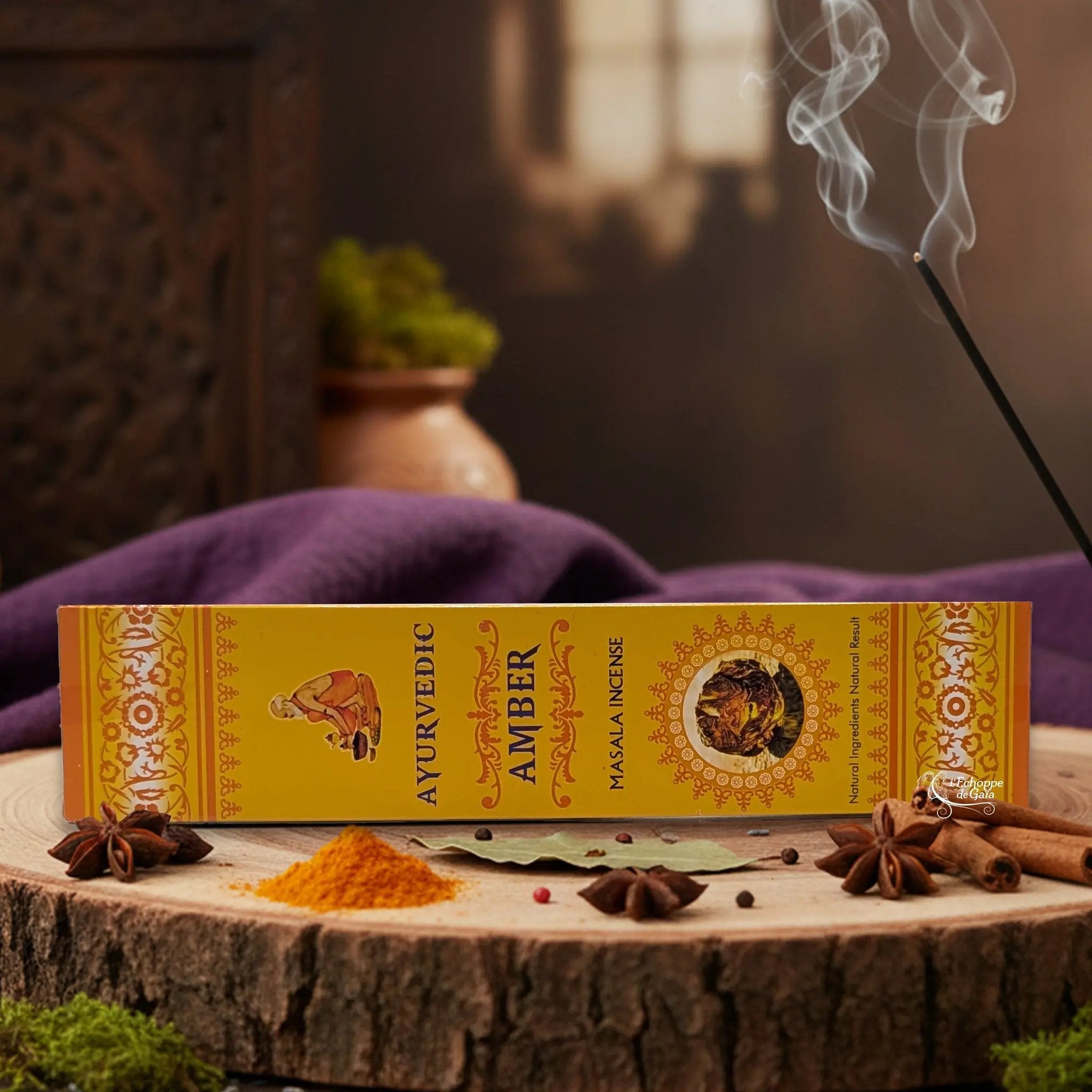 Boîte d'encens "Ayurvedic Amber Masala" sur une rondelle de bois, avec épices et encens fumant.