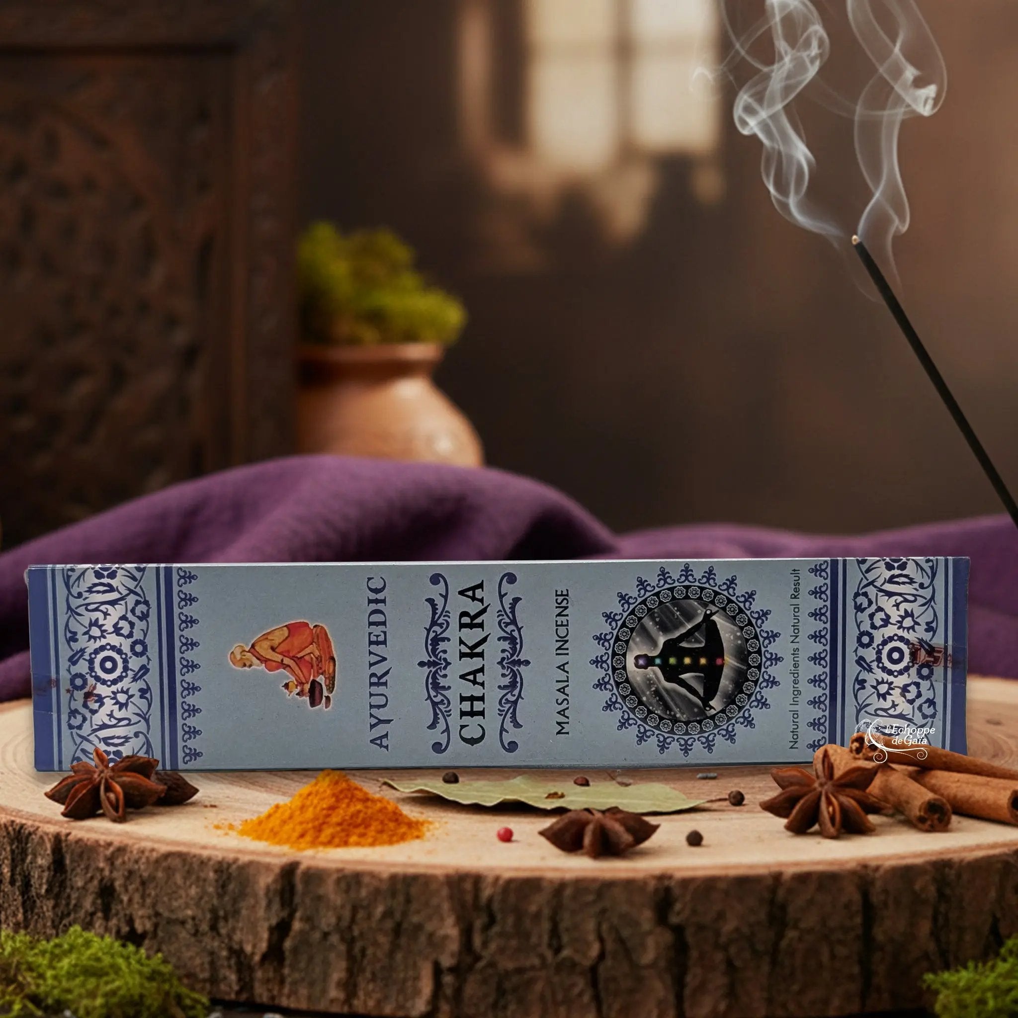 Boîte d'encens "Ayurvedic Chakra Masala" sur une rondelle de bois, avec épices et encens fumant.