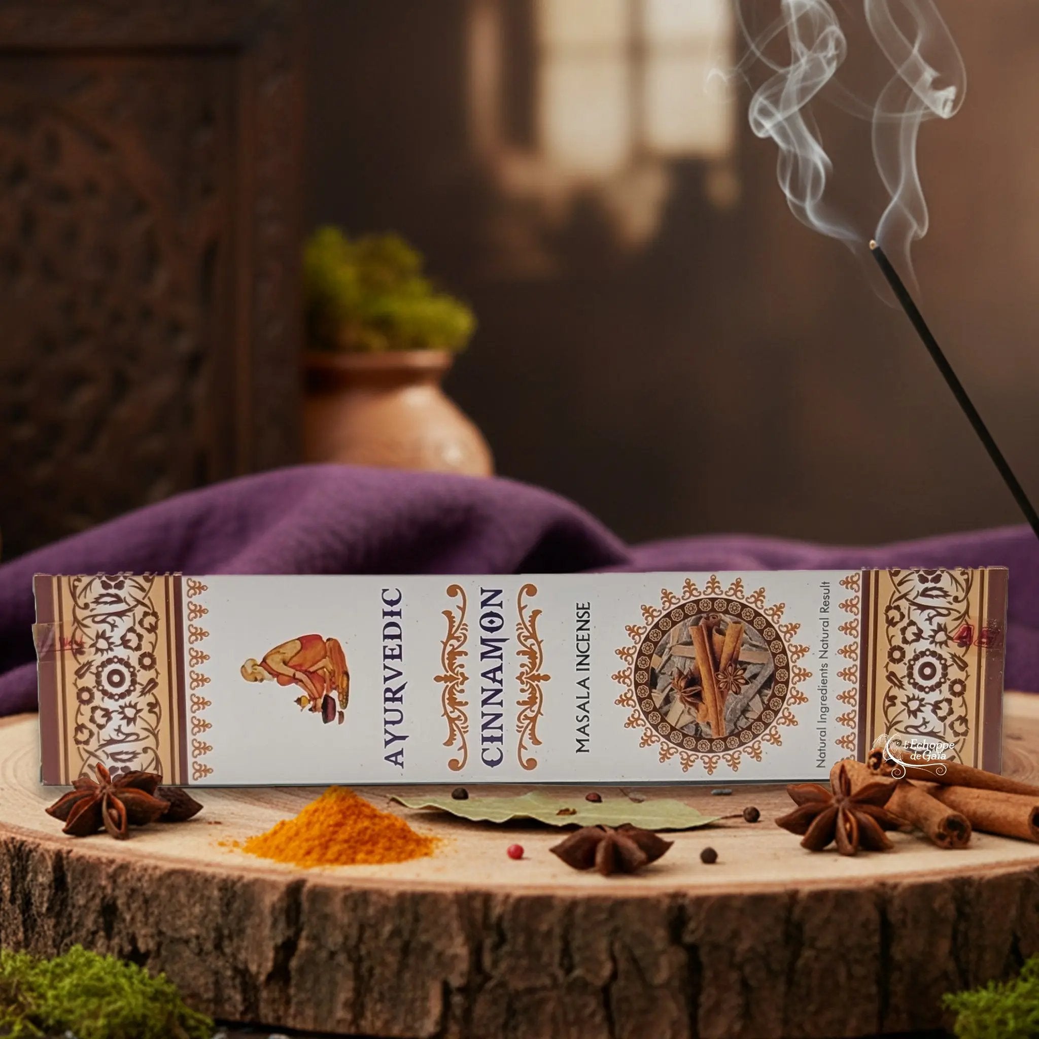 Boîte d'encens "Ayurvedic Cinnamon Masala" sur une rondelle de bois, avec épices et encens fumant.
