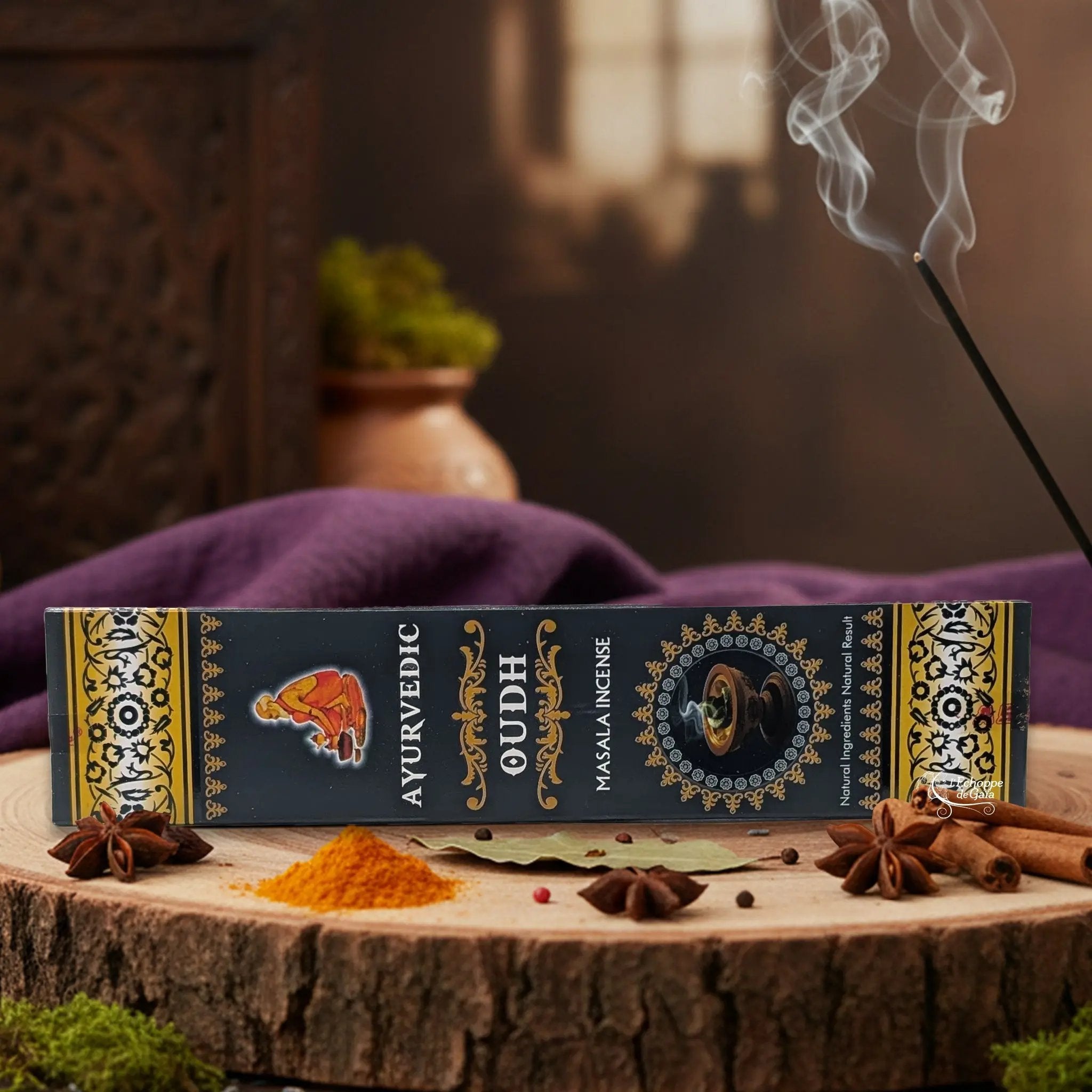 Boîte d'encens "Ayurvedic Oudh Masala" sur une rondelle de bois, avec épices et encens fumant.